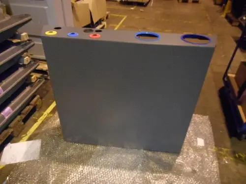 Graue Verkleidung mit vier ausgehöhlten Bereichen an der Oberseite, gelb, blau, rot und schwarz markiert. Produkt von Remeha, auf einem Schutzmaterial in einer Lagerumgebung platziert.